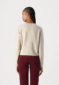 Beige ullgenser med rund hals, ribbede mansjetter og hem, kombinert med burgunder kordfløyelsbukser med baklommer.