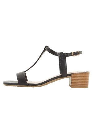 Black leather sandal with a T-strap design, ankle buckle, and wooden block heel. Features a flat sole and minimalistic accents.