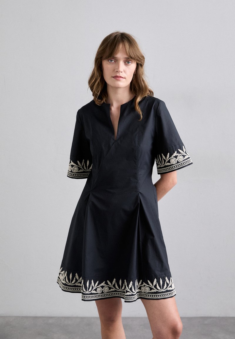 Vestido negro con falda plisada, mangas cortas y cuello con abertura. Presenta intrincados bordados blancos a lo largo de las mangas y el dobladillo.
