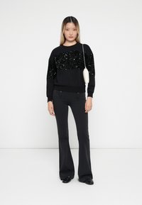 Sweatshirt preto com um detalhe em lantejoulas na parte superior do peito, combinado com calças pretas flare. O conjunto apresenta um design elegante e uma silhueta ajustada.