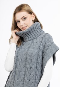 Graues gestricktes Poncho mit hochgeripptem Kragen und kurzen Ärmeln, versehen mit einem strukturierten Kabelmuster.