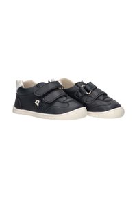 Zapatos sintéticos negros con dos correas de Velcro, de forma redondeada, suela de goma blanca, con un pequeño detalle de logo en el lateral.