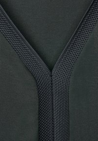 Una tela de color verde oscuro presenta un diseño texturizado en forma de V. El escote cuenta con un patrón de punto en contraste, que resalta una mezcla de superficies lisas y texturizadas.