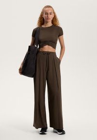 Top scurt maro cu detalii pliate; pantaloni maroc loose-fit cu șnur; geantă de umăr neagră. Încălțăminte sport casual.
