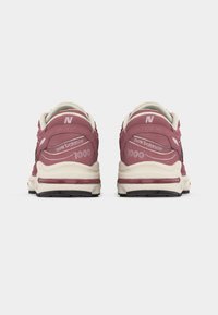 Ζευγάρι ροζ και λευκών αθλητικών παπουτσιών New Balance 1000, εμφανιζόμενα από το πίσω μέρος πάνω σε απλό λευκό φόντο.