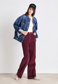 Τζάκετ τζιν, λευκή μπλούζα, μπορντό παντελόνι καμπάνα από κοτλέ, γκρι μπαλαρίνες, μαύρο καπέλο με λογότυπο. Χαλαρό ντύσιμο με αντιθετικές υφές και χρώματα.