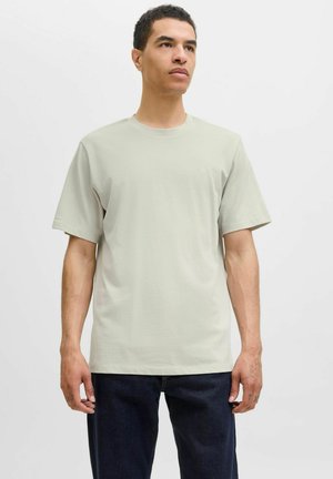 Hellgraues Baumwoll-T-Shirt mit Rundhalsausschnitt und kurzen Ärmeln, mit einem dezenten Logo auf der Brust und einem lässigen Schnitt. Getragen mit dunklen Jeans.