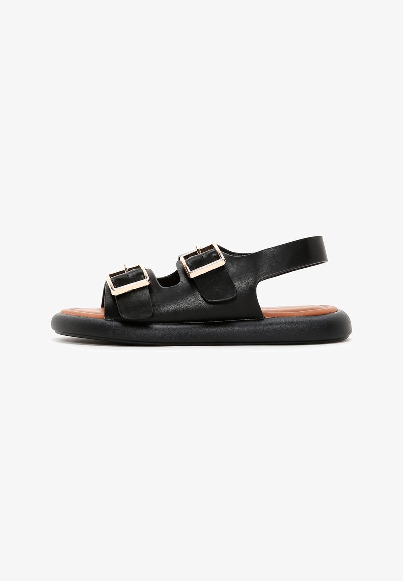 Black leather sandals with two buckle straps, open toe, and back strap. Textured black sole, contrasting tan footbed.