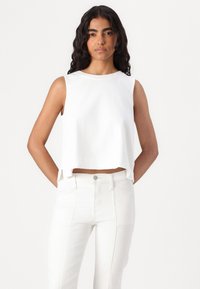 Biely crop top vyrobený z bavlny, s okrúhlym výstrihom a bezrukávovým dizajnom, s bočnými rozparkami pre extra detail.