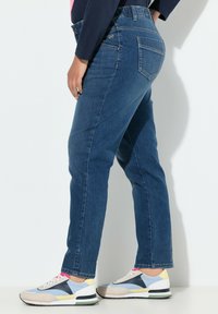 Jean de mezclilla azul con un diseño de pierna recta, que cuenta con un bolsillo trasero y una textura suave. Combinado con zapatillas de colores múltiples.