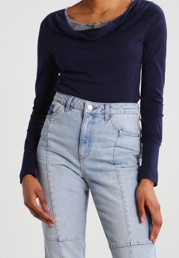Dunkelblaues Langarmshirt mit rundem Ausschnitt über einer gemusterten Schicht, kombiniert mit hell gewaschenen Jeans mit Patchwork-Details.