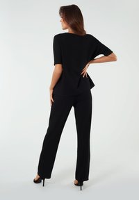 Czarny strój składający się z koszulki z krótkim rękawem z rozcięciem z tyłu, zestawiony z dopasowanymi spodniami prostymi oraz butami na wysokim obcasie. Gładka tekstura.