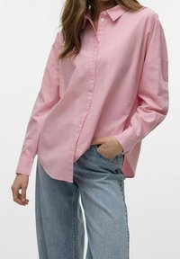 Camisa de botones de un suave color rosa claro con cuello, de corte relajado y mangas largas, combinada con jeans de pierna ancha en un ligero tono azul. Tejido de algodón suave.