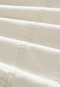 Gros plan d'un tissu crème avec des coutures parallèles courant horizontalement à travers un matériau doucement plié.