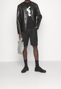 Black leather jacket, black graphic t-shirt, tailored black shorts, gray bag, black socks, and shoes with a textured sole.