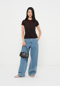 Zwarte kant peplum top met korte mouwen, gelaagd over een bruine shirt, gecombineerd met lichtblauwe wijde jeans en een zwarte handtas.