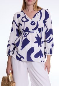 Witte blouse met abstracte marineblauwe patronen. Heeft een V-hals, lange pofmouwen en een strikdetail bij de halslijn. Lichtgewicht stof.