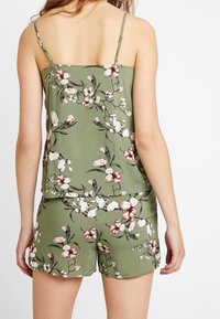 Zielony top bez rękawów w kwiatowy wzór z regulowanymi ramiączkami, w zestawie z pasującymi szortami. Posiada białe i różowe akcenty kwiatowe.