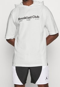 Witte katoenen hoodie met korte mouwen, voorzien van de tekst "Breakfast Club", een capuchon en opvallende graphics. Draag met zwart-witte shorts.