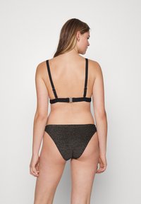 Top de bikini preto com alças ajustáveis e fecho nas costas, combinado com calções de bikini de cintura baixa e brilho. Apresenta um design simples e uma textura suave.