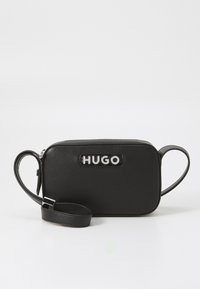 Svart lær rektangulær bag med en sølv "HUGO"-logo, glidelås lukking og avtakbar stropp for allsidige bæringsalternativer.