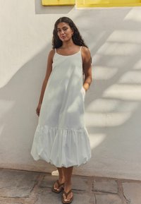 Heled beez dress õhukeste rihmadega, millel on lai, volangiline äär. Sile, tekstuuriga kangas ulatub keskel veille. Kanda pruunide plätudega.
