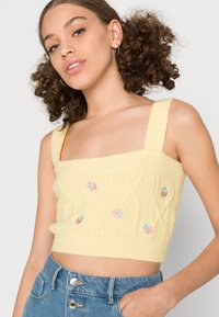 Top de malha cropped amarelo com decote quadrado, alças largas e bordado floral rosa. Apresenta um padrão de cabos em forma de diamante texturizado.