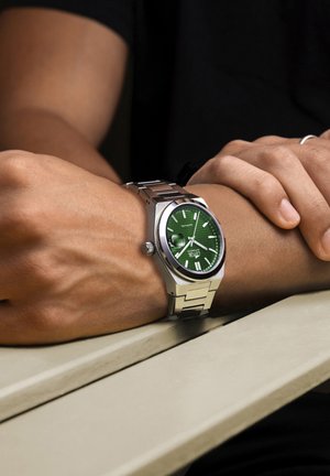 Montre argentée avec un cadran vert et des index blancs, dotée d'un bracelet en acier inoxydable et d'un cadran texturé pour un contraste visuel.