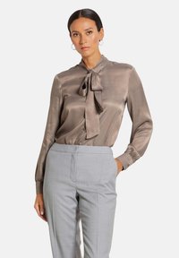 Zijden blouse in taupe met een strik halslijn, lange mouwen en knoopmanchetten, gecombineerd met lichtgrijze op maat gemaakte broek. Soepele textuur en elegante ontwerp.