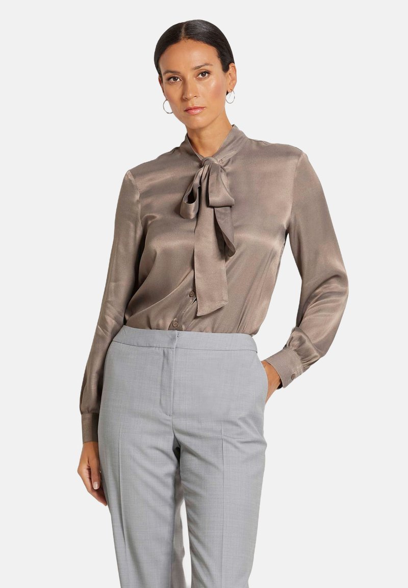 Zijden blouse in taupe met een strik halslijn, lange mouwen en knoopmanchetten, gecombineerd met lichtgrijze op maat gemaakte broek. Soepele textuur en elegante ontwerp.