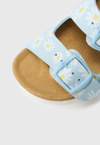 Modre sandale z vzorcem cvetja, z dvema nastavljivima trakovoma, pluto podplatom in belim podplatom. Na zgornjem delu so marjetice z rumenimi središči.