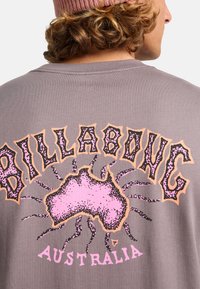 Szara bawełniana koszulka z dużą różową grafiką Australii z czarnymi akcentami oraz napisem "BILLABONG AUSTRALIA" w wyraźnym kroju pisma.