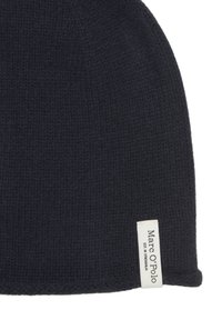 Donkerblauwe muts gemaakt van getextureerde gebreide stof, met een wit label met "Marc O'Polo" bij de boord. Zacht en warm ontwerp.