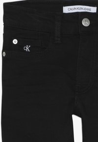 Jeans de mezclilla negros con una textura suave, que cuentan con un botón plateado, un bolsillo lateral con el logo 'ck' y costuras de contraste en los bolsillos.