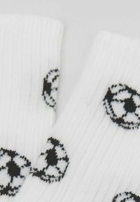 Bílé ponožky s černobílým vzorem fotbalového míče, vyrobené z ribového materiálu s jemnou texturou a elastickými otvory.