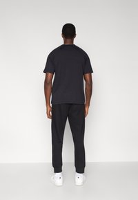 Czarna koszulka z krótkim rękawem i okrągłym dekoltem, w zestawie z czarnymi spodniami dresowymi z elastycznymi mankietami oraz białymi trampkami.