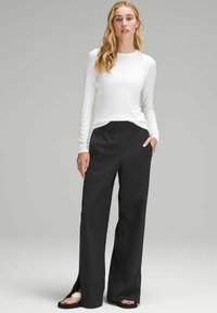 Top bianco a maniche lunghe abbinato a pantaloni neri a gamba larga con spacchi laterali. Tessuto testurizzato con una vestibilità leggera e rilassata.