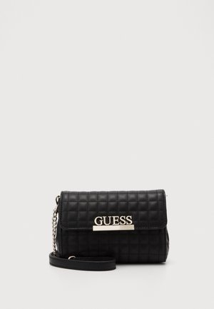 Bolso bandolera negro de piel acolchada con cadena plateada y logotipo "GUESS" en la solapa frontal.