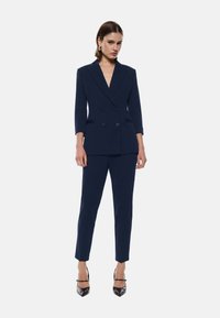 Abito blu navy su misura con giacca doppiopetto a maniche tre quarti e pantaloni slim fit; texture liscia e senza motivi.