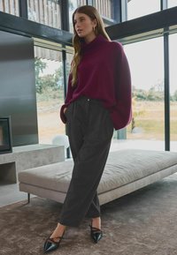 Bordeaux turtleneck trui, ruime pasvorm, gecombineerd met donkergrijze high-waisted broeken en zwarte puntige flats op een luxueus beige tapijt.