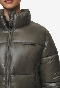 Gevoerde pufferjas in olijfgroen. Voorzien van een hoge kraag, ritssluiting aan de voorkant en "PEGADOR"-logo. Gladde, glanzende afwerking met gestikte details.