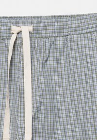 Pantalon en tissu à carreaux verts et bleus avec une taille élastique et un cordon blanc cassé noué au centre devant.