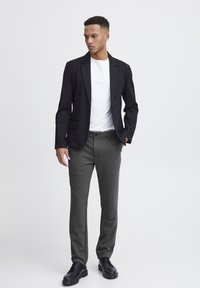 Black blazer over a white t-shirt, paired with dark gray trousers and black shoes. The fabric appears smooth and tailored.