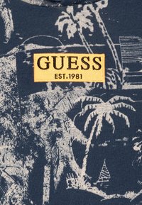 Granatowa bawełniana bluza z kapturem z białą grafiką palmy oraz żółtym prostokątnym logo "GUESS EST.1981" na piersi. Miękka w dotyku.