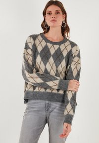 Sivi in krem pulover s argyle vzorcem, okroglim izrezom, ohlapnim krojem in rebrastim robom. Mehka tekstura s kontrastnimi diamantnimi oblikami.