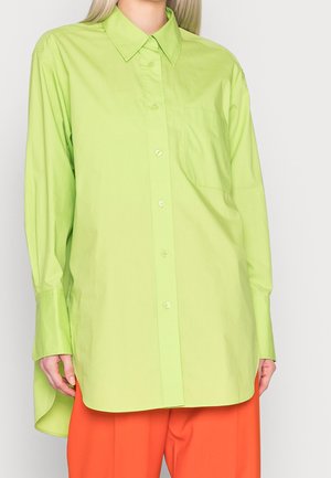 Femme portant une chemise boutonnée oversize vert citron avec une poche poitrine et un pantalon large orange vif.