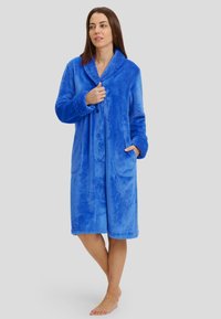 Bata de felpa azul con cuello chal, mangas largas, dos bolsillos frontales y cierre de botón. Textura suave y diseño hasta la rodilla.