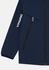 Veste bleu marine en tissu lisse, dotée de poches zippées noires, de poignets élastiques et d'un logo blanc sur la manche.