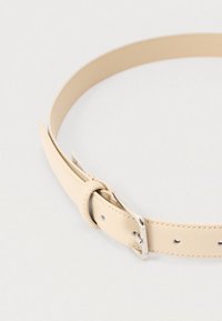 Cinturón de cuero beige con textura suave, diseño delgado y hebilla de metal plateada. Cuenta con varios orificios de ajuste a lo largo de la correa.