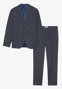 Completo in tessuto a quadri navy con giacca su misura a due bottoni, rever a taglio e pantaloni a gamba dritta. Fodera in satin liscia visibile.